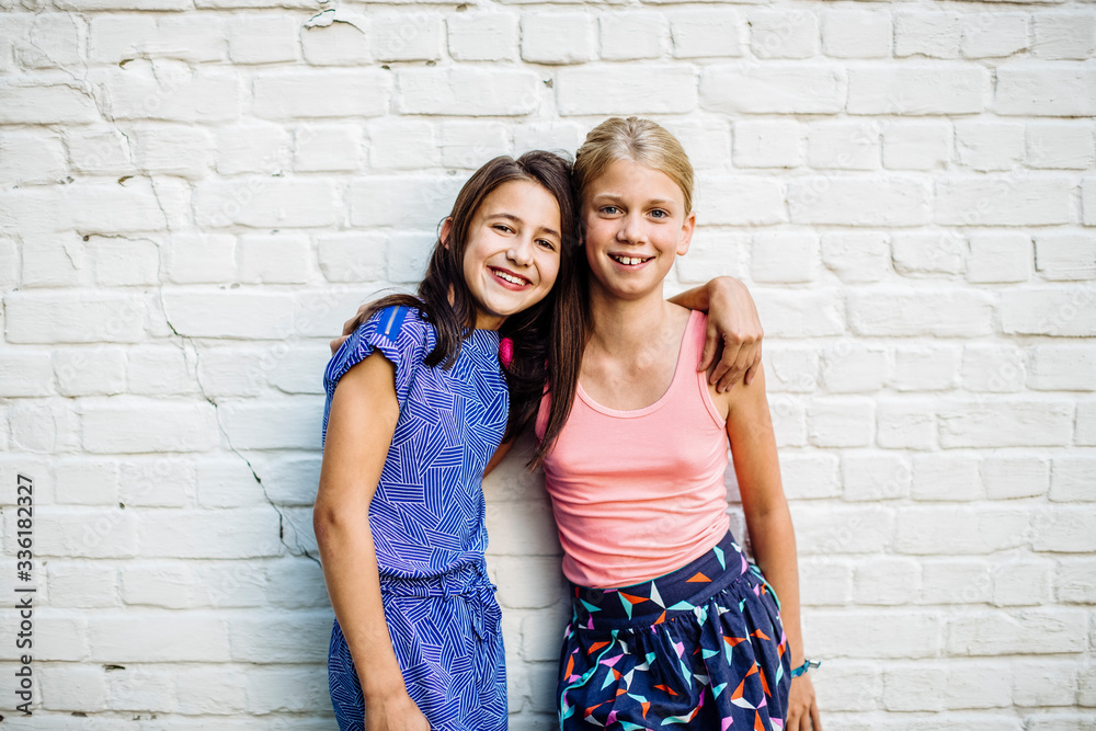 Portrait of two happy girls embracing at a wall Stock Photo | Adobe Stock
