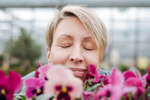 Smiling Woman Smelling On Pansies In Flower Shop