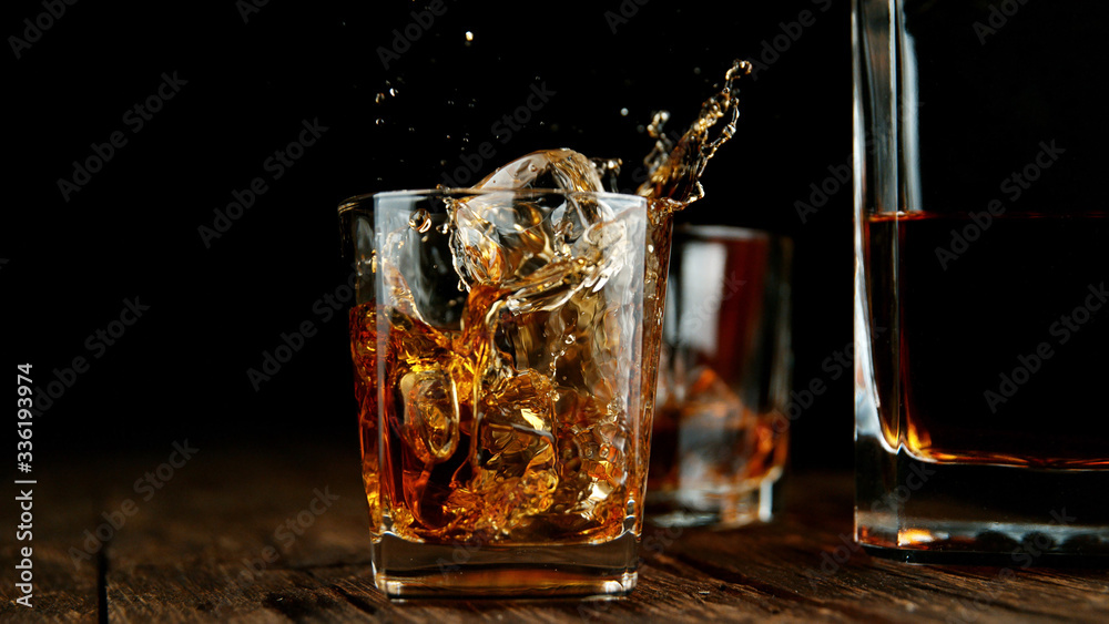 Splashing whiskey from glass with ice cubes inside - obrazy, fototapety, plakaty 
