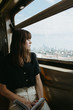 © KATIE + JOE/Stocksy - Woman with bangs sitting on a train and looking out the window at the city in the distance