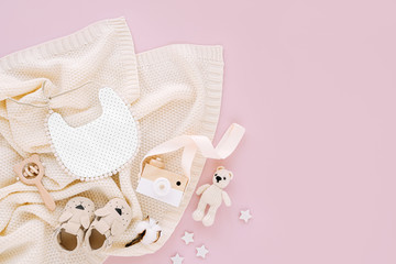 Set of clothes and accessories fot newborn. Toys, bib  and baby slippers with knitted blanket on pink background. Baby shower concept.    Flat lay, top view