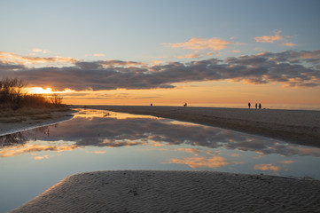 Calm evening by the seaside, people walking by the sea shore, sunset reflecting in the water
