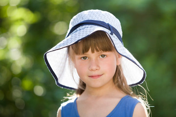 Wall Mural - Close-up portrait of happy smiling little girl in a big hat. Child having fun time outdoors in summer.