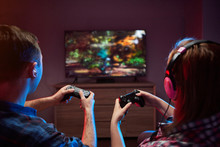 Portrait Of Crazy Playful Couple, Gamers Enjoying Playing Video Games On Playstation Indoors Sitting On The Sofa, Holding Console Gamepad In Hands, Xbox Fans. Resting At Home, Have A Great Weekend
