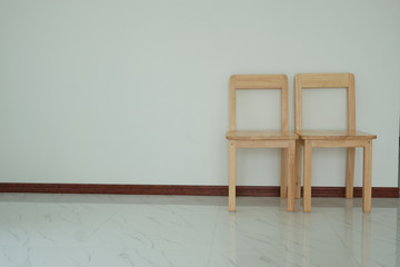 Two wooden chair is located in the empty room on the white wall.