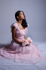 South Asian woman sits on the floor in a pink dress with flowers in her hands