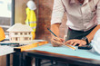 © Charnchai saeheng - engineers holding a pen pointing to a building and  drawing outlay construction plan as guide for builders with details