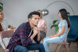 © zinkevych - Young man in a checkered shirt sitting with colleagues and looking thoughtful