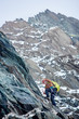 © anatoliy_gleb - Mountaineer with backpack using fixed rope to climb high rocky mountain. Man climber ascending alpine ridge and trying to reach mountaintop. Concept of mountaineering and alpine rock climbing.