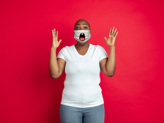 Astonished. Portrait of young african-american woman with emotion on her protective face mask isolated on studio background. Beautiful female model. Human emotions, facial expression, sales, ad