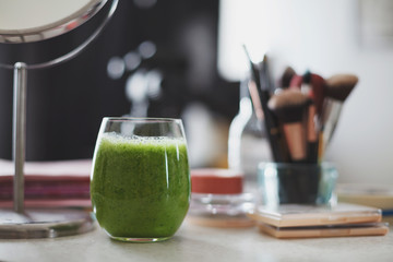 Transparent glass filled with green smoothie on makeup table.