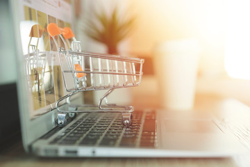 Online shopping concept, Shopping cart with blurry laptop on the desk