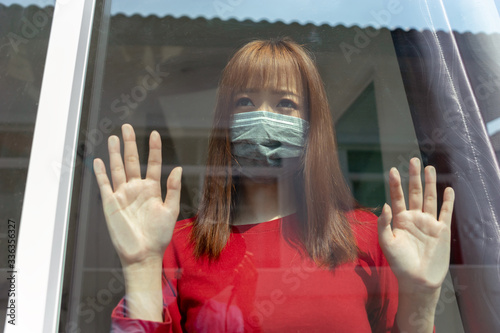 Coronavirus, covid-19 of Asian woman patient wearing mask quarantine stay at home to prevent the germs from spreading to people looking through the window, Self isolation from society to reduce risks.