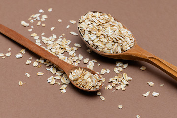 oat flakes in a two wooden spoon on a brown background