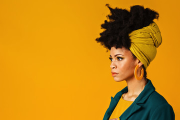 Wall Mural - Profile portrait of a serious young woman with big yellow earrings and afro hair wrapped with head wrap scarf