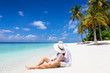 Ein Paar in weißer Sommerkleidung sitzt am tropischen Paradies Strand mit Palmem und türkisem meer und genießt den Urlaub