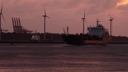 Wall Mural - Cargo ship entering the Port of Rotterdam during twilight light glow after sunset, oil silos and wind turbines in the background