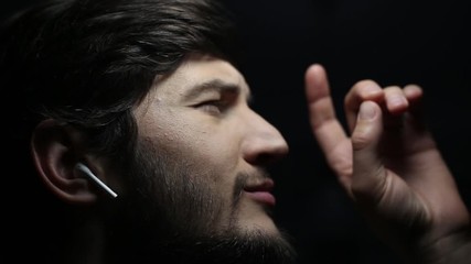 Wall Mural - Dark close-up portrait of young man with wireless earphones on black background.