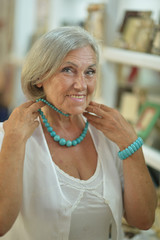 Sticker - Beautiful smiling senior woman at souvenir store trying on necklace