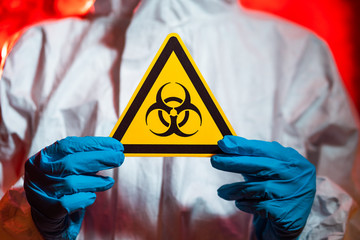 A doctor in a protective suit holds a biohazard sign. Coronavirus pandemic concept, quarantine