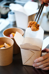 Poster - Tweezers holding deep-fried asian cooked piece of chicken above the delivery boxes, vertical