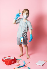 Personal protective equipment: a little boy in a medical mask and blue gloves plays with a children's set of a doctor.