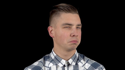 A young man shows emotion a contemptuous look on his face. A man with a scornful look in a shirt on a black background closeup