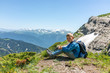 © Dmitrii Potashkin - A boy traveler with hiking poles and a backpack is resting in the summer on top of a mountain with snow.