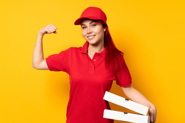 Pizza delivery girl holding a pizza over isolated background doing strong gesture