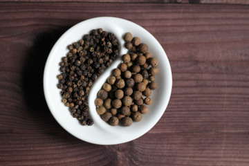 Canvas Print - Black pepper corns and allspice  in Yin Yang shaped bowl on wooden background