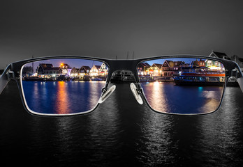 Wall Mural - Black metal glasses looking through colorful night cityscape. Glasses for people with visual impairment. Color blindness. World perception. Medical condition. Health and disease concept. Colorblind.