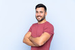© luismolinero - Young handsome man with beard over isolated blue background with arms crossed and looking forward