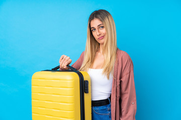 Young Uruguayan woman over isolated blue background in vacation with travel suitcase and unhappy