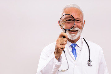 Portrait of senior doctor doctor with loupe on gray background.