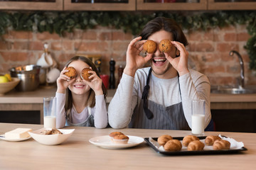 Father and daughter having fun in kitchen, making cupcake eyes