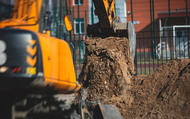 Wall Mural - Yellow heavy excavator excavating sand and working during road works, unloading sand during construction of the new road with workers around