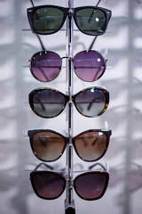 Wall Mural - A row of glasses to protect from the sun. Store points. Stand with sunglasses in the optics store. Female hand shows glasses. Presentation of points. Close-up