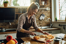 Happy Woman Slicing Bread With A Knife While Preparing Food In The Kitchen.