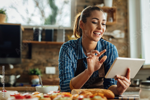 Fotografía Young happy woman using digital tablet while preparing food in the kitchen