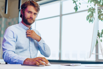 Wall Mural - Young bearded businessman using his computer in a modern office place. Business concept