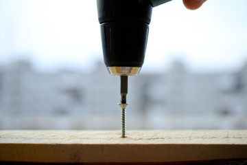 An electric screwdriver is ready to screw a screw into a wooden board