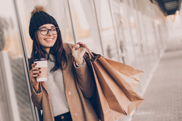 Beautiful fashionable woman drink coffee walking near mall with shopping bags.