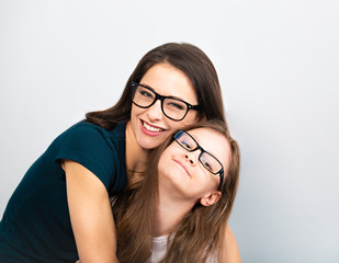 Wall Mural - Young casual toothy smiling mother and happy kid in glasses hugging on light blue background. Closeup studio portrait. Teaching kids staying at home. Online education.