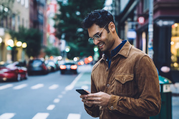 smiling ethnic young man in jacket chatting on street
