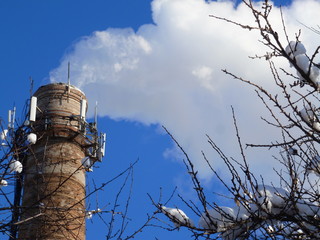 Pipes of an old factory throw clouds of poisonous white smoke into the sky polluting the atmosphere. Urban smog from smoke from boiler houses. White smoke from a chimney against a blue clear sky.