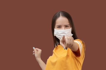 Wall Mural - Coronavirus Prevention Protection against viruses and diseases, health products. Girl in antibacterial medical mask shows you, isolated on brown background