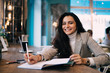 © BullRun - Portrait of toothy woman smiling at camera during time for exam preparation and learning in public coffee shop, happy female student studying information while doing university homework in textbook