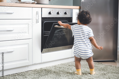 Little African-American baby near stove in kitchen Poster Mural XXL