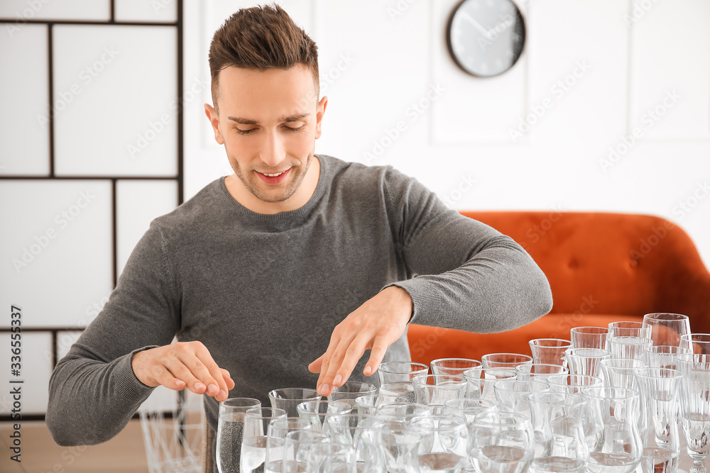 Young man playing music on glasses with water at home