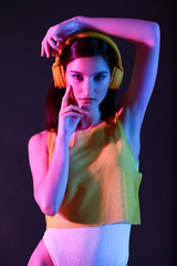 Wall Mural - Toned portrait of beautiful young woman with headphones on dark background